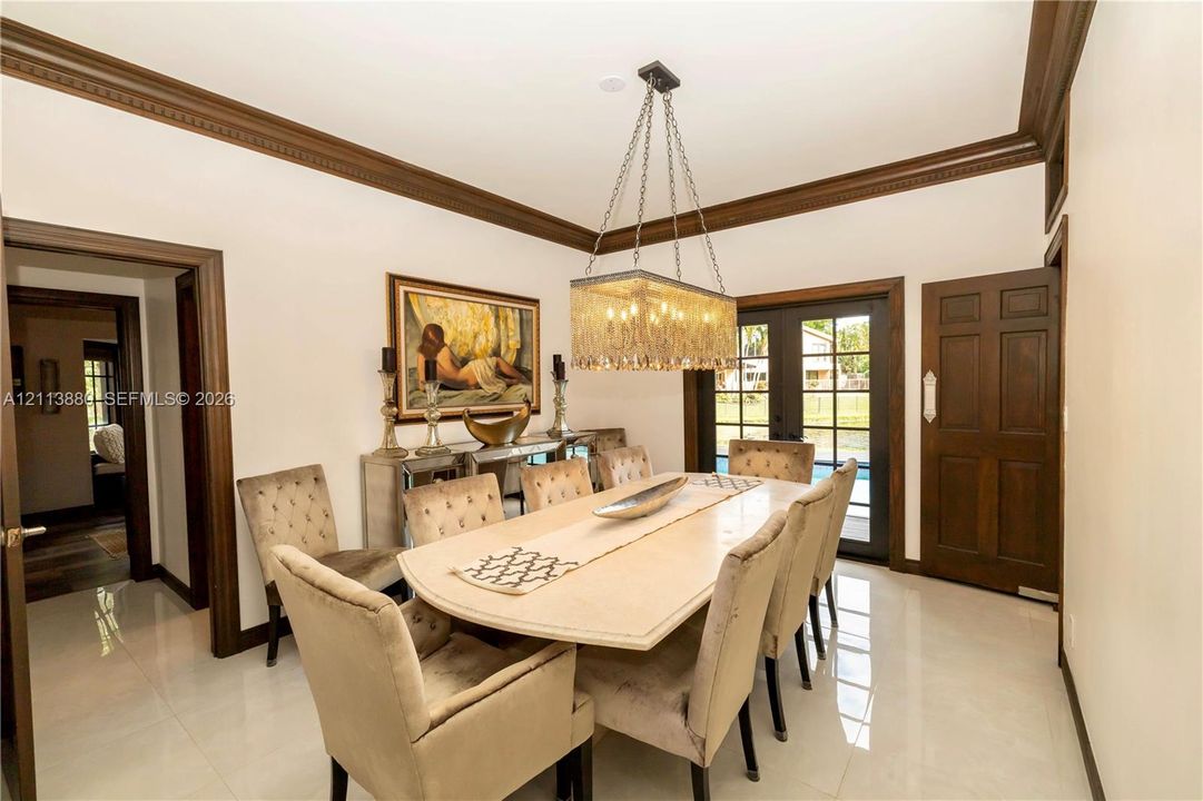 Dining area featuring high-gloss tile flooring, crown molding, a rectangular tiered crystal chandelier, and a six-panel wood door