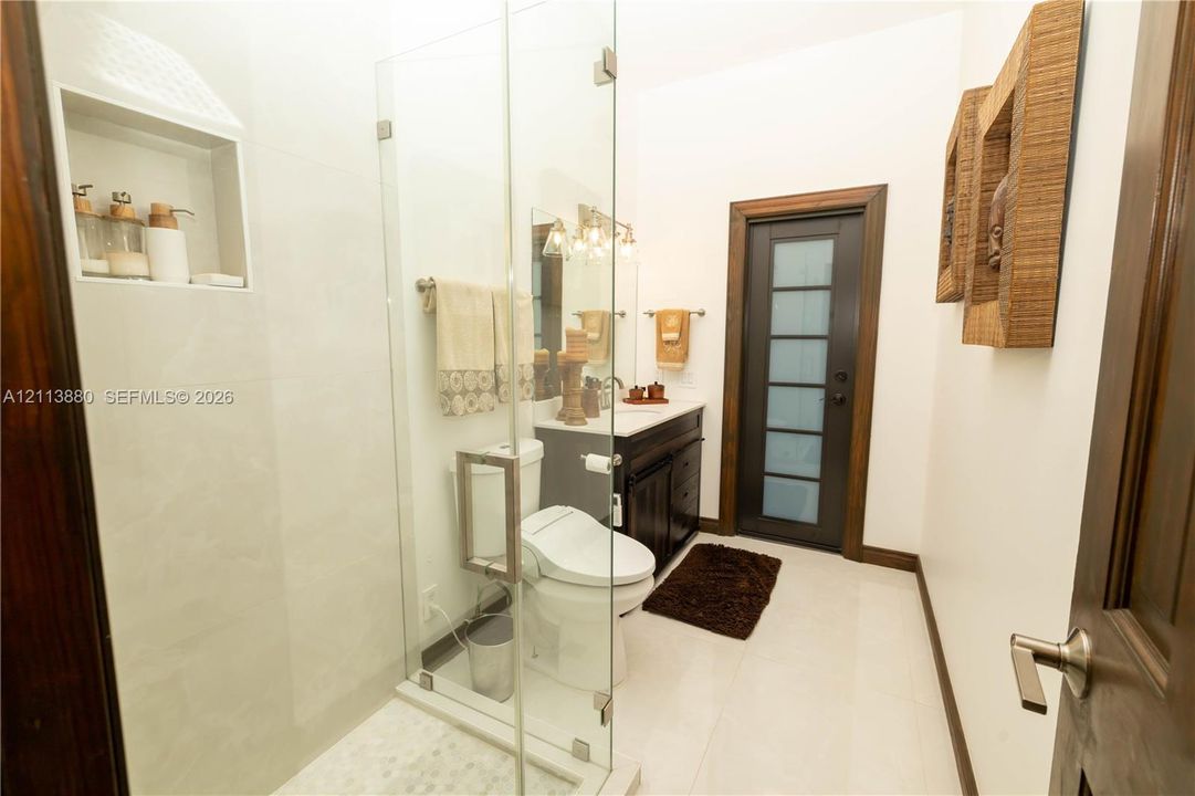 Frameless glass shower enclosure with built-in tile niche, dark wood cabinetry, and a door with frosted glass paneling