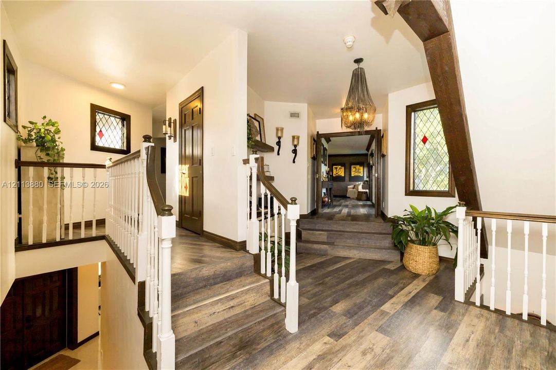 Foyer featuring wood-finish flooring, white spindle railings, decorative leaded glass windows, exposed structural timber beams, and a tiered staircase