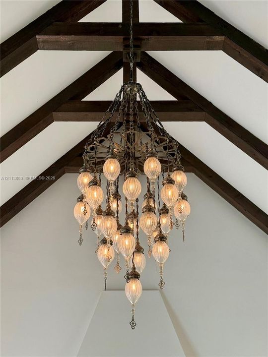 Vaulted ceiling featuring exposed timber beams and a multi-tiered metal chandelier with scalloped glass fixtures