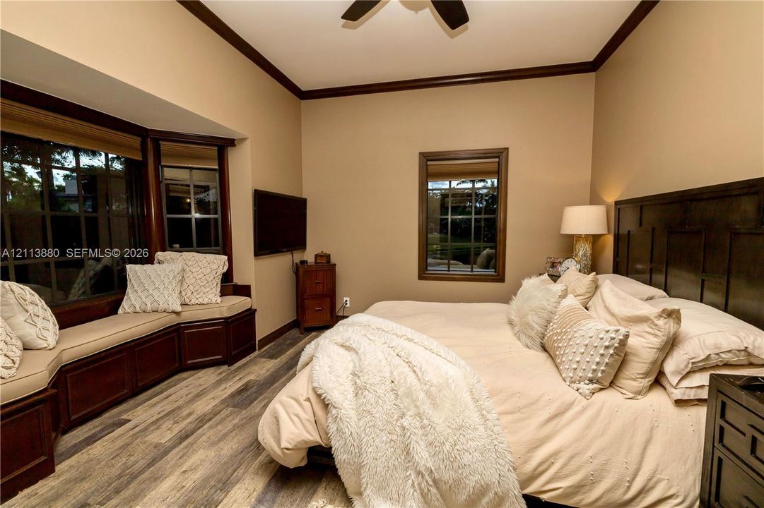 Bay window with built-in bench seating, wood-finish flooring, dark wood-tone crown molding, and grid-pattern window panes
