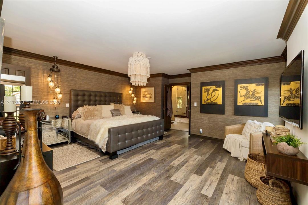 Textured wall coverings, wood-finish flooring, crown molding, tiered chandelier, and multi-light pendant fixture