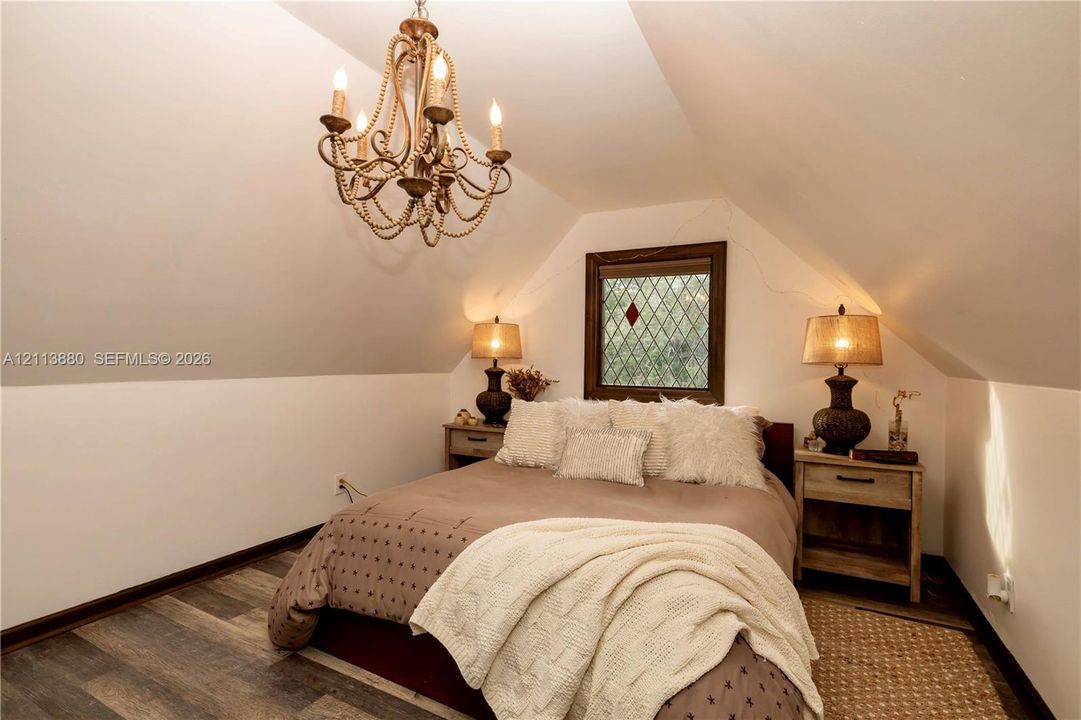 Sloped ceiling room featuring wood-finish flooring, a decorative beaded chandelier, and a leaded glass window with a dark wood frame