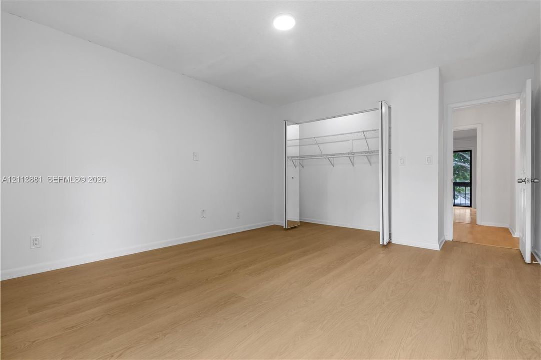 Neutral-toned interior featuring wood-finish flooring, white walls, flush-mount ceiling lighting, and a closet with bifold doors and wire shelving