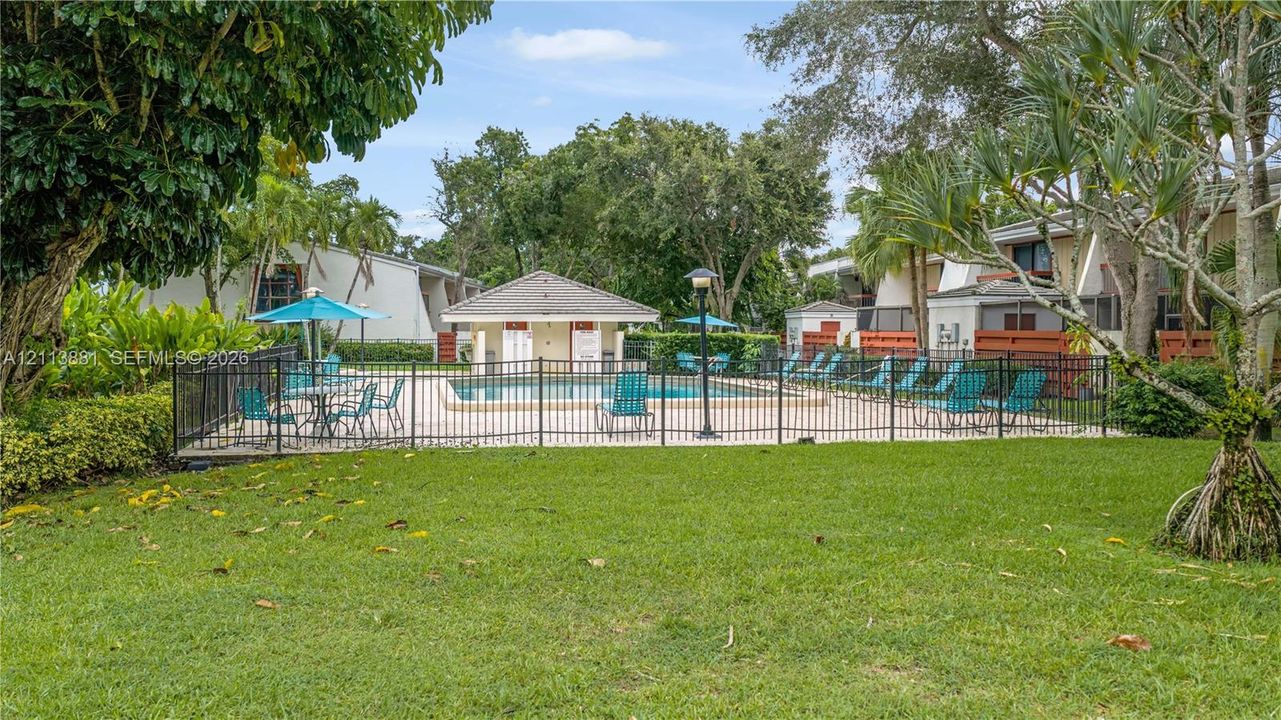 Outdoor recreation area featuring an in-ground swimming pool, a covered pool house, perimeter metal fencing, and landscaped grounds