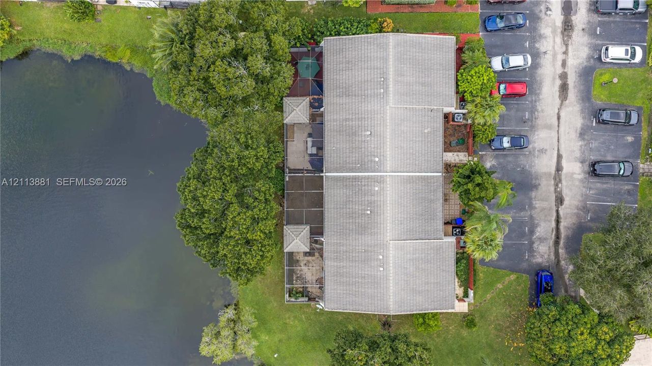 Aerial perspective of a multi-unit property featuring water frontage, an expansive screened-in patio area, mature trees, and designated surface parking