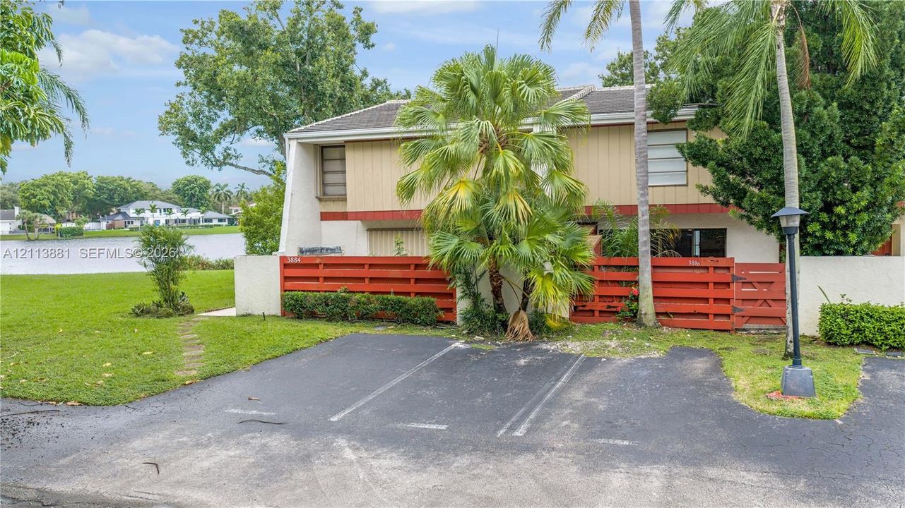 Two-story structure featuring a dual-tone exterior, red horizontal wood privacy fencing, private asphalt parking, and a shoreline location
