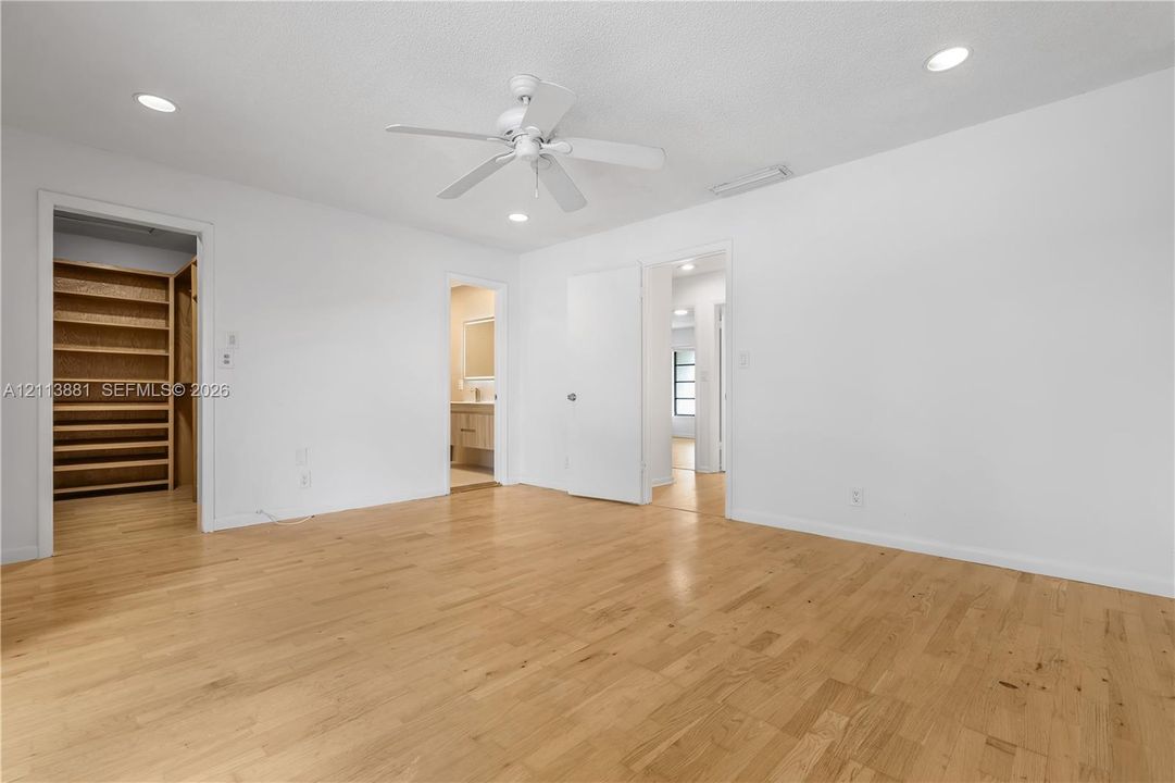 Interior room featuring wood-finish flooring, recessed lighting, white ceiling fan, and built-in closet shelving
