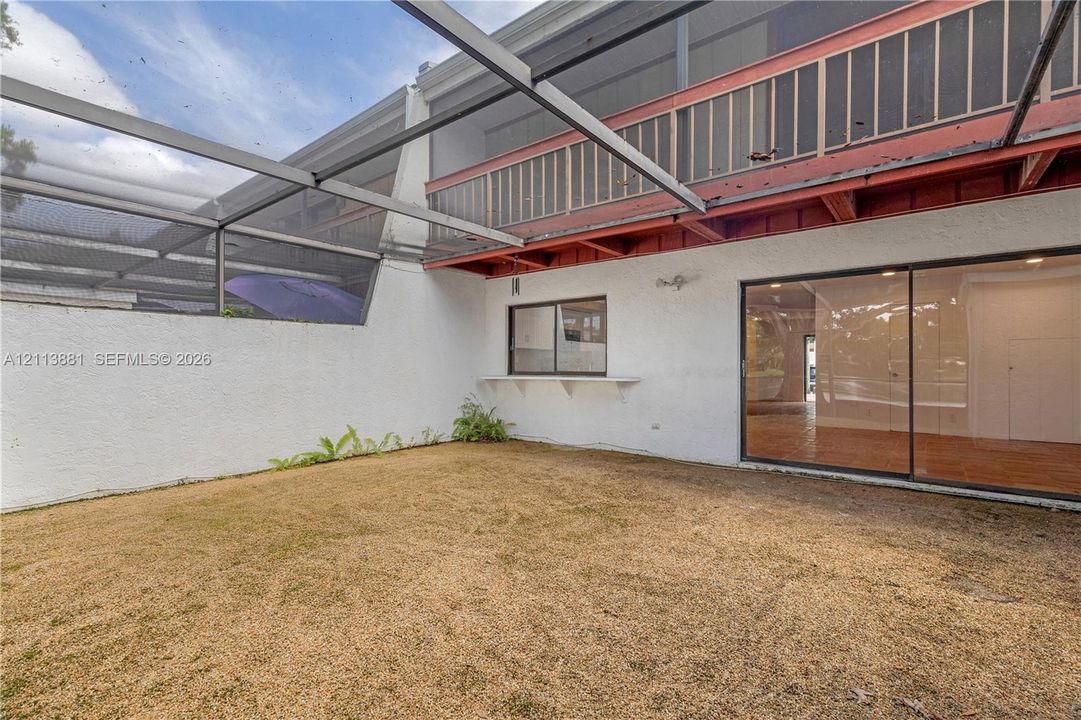 Screened outdoor area featuring a stucco wall, an upper-level balcony with a railing, and large sliding glass doors