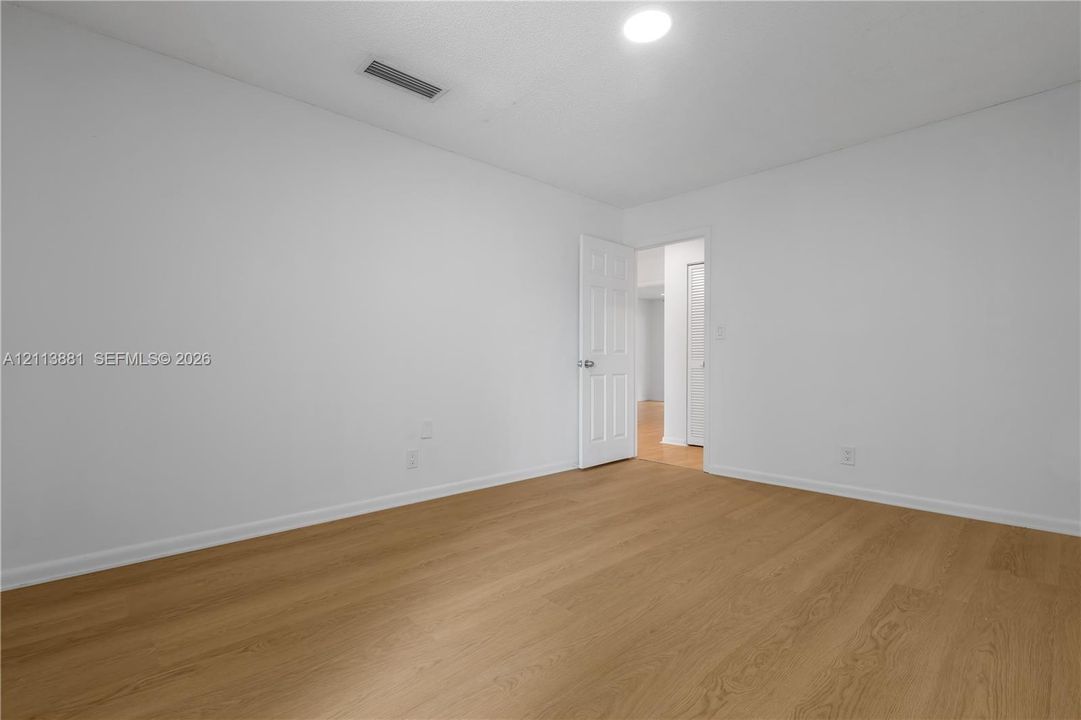 Neutral interior space featuring wood-finish flooring, white walls, and a multi-panel door