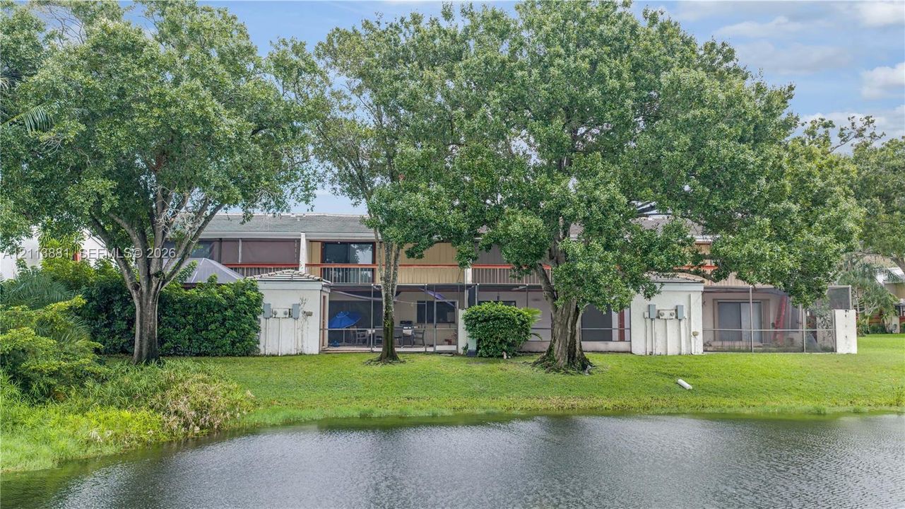 Exterior featuring waterfront positioning, multiple screened-in ground-level lanais, second-story balconies, and mature canopy trees
