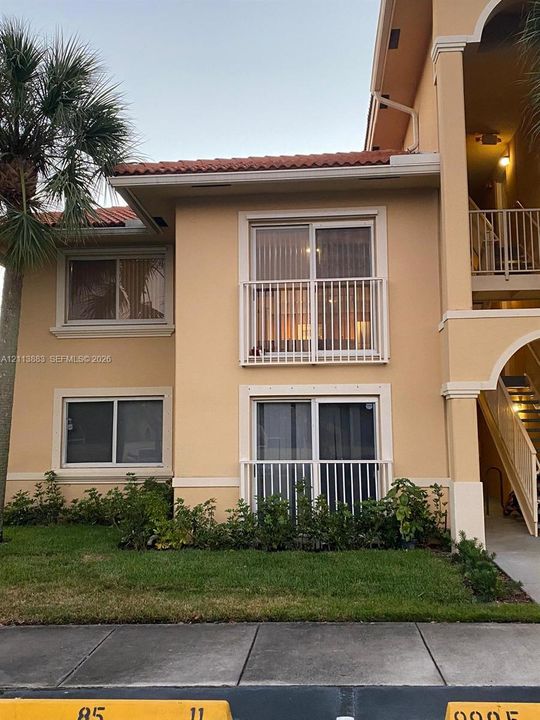 Exterior facade featuring stucco siding, mission-style tile roof, metal railing balconies, and sliding glass entry doors