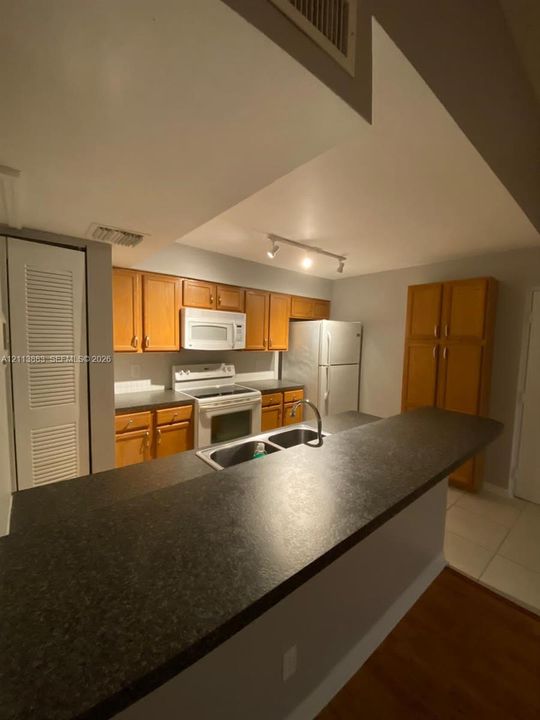 Kitchen featuring wood cabinetry, dark solid-surface countertops, dual-basin sink, integrated track lighting, and a tall built-in pantry
