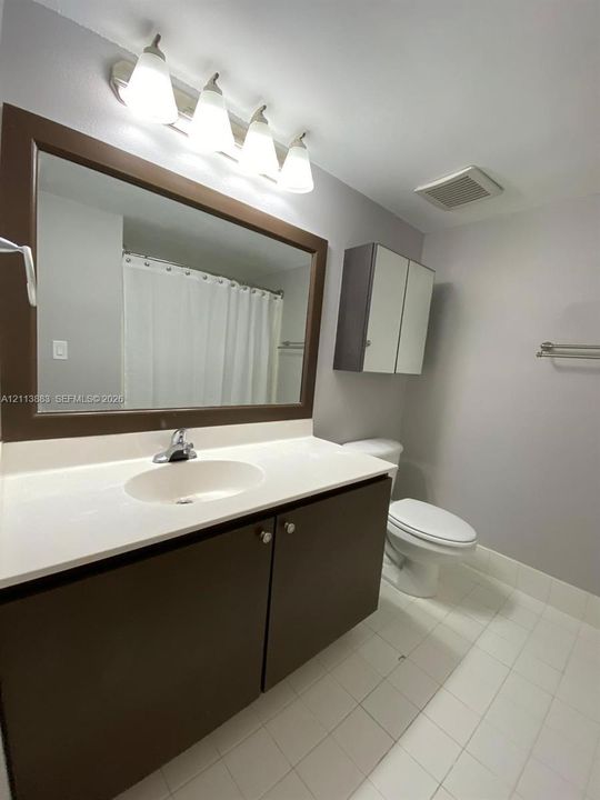 Bathroom featuring a vanity with a solid-surface countertop, an integrated sink, a framed mirror, wall-mounted cabinetry, and a four-light fixture
