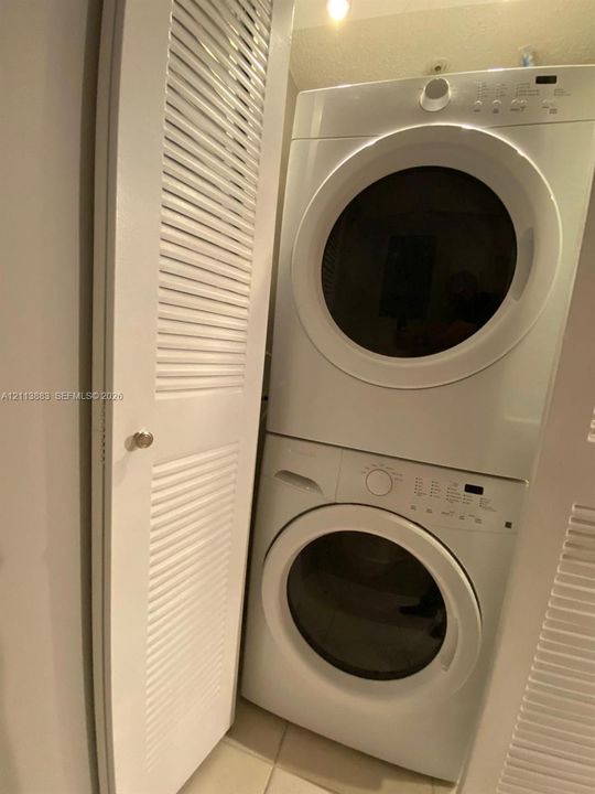 Stacked washer and dryer unit enclosed by white louvered doors