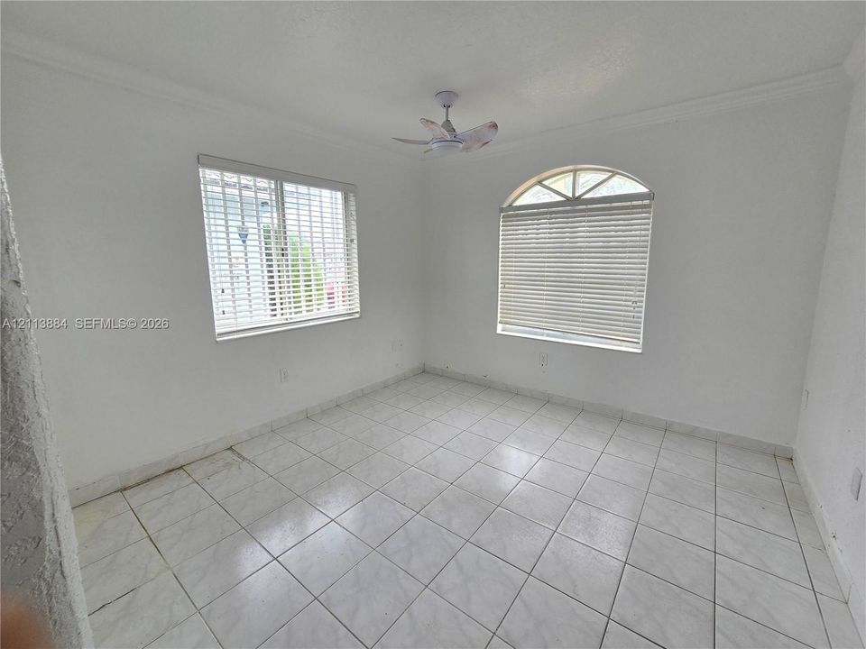Room featuring white ceramic tile flooring, an arched window, a ceiling fan, and crisp crown molding