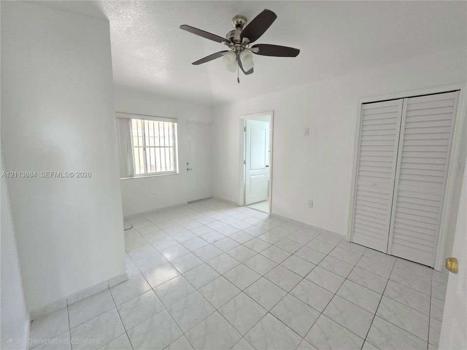 Interior room featuring tile flooring, ceiling fan with light fixture, louvered closet doors, and multi-pane window