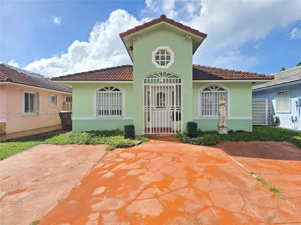Stucco exterior with a central gable, tiled roof, arched windows featuring security grilles, and a stained concrete driveway
