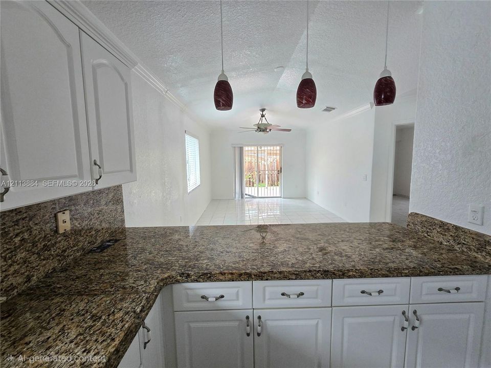 Kitchen featuring white shaker-style cabinetry, stone-finish countertops, three suspended pendant lights, and tile flooring