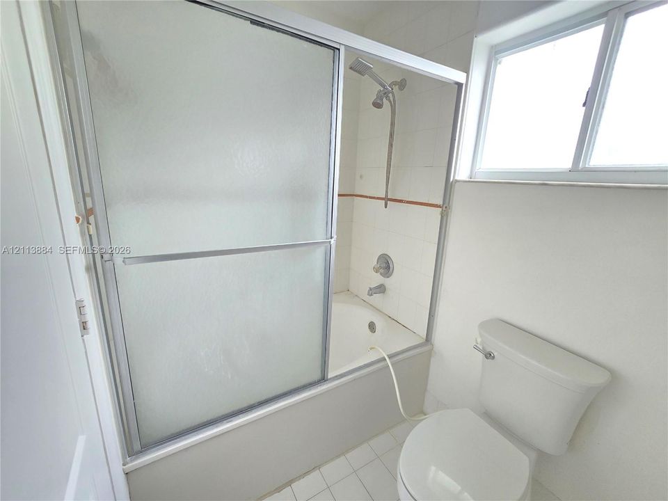 Bathtub and shower combination featuring sliding textured glass doors, tiled surround, wall-mounted shower head, and white floor tiling