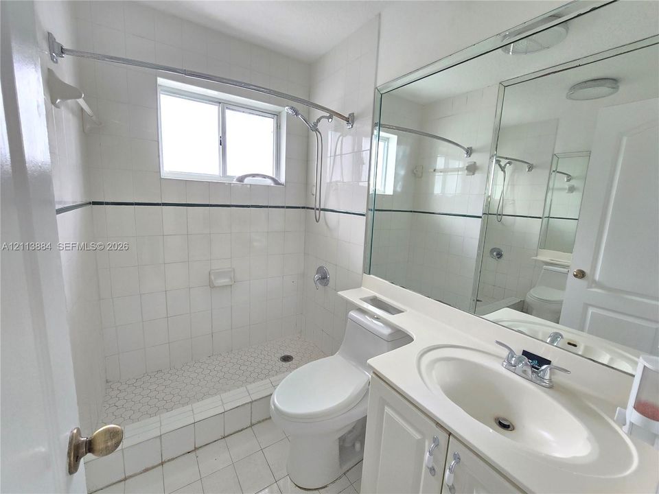 Bathroom featuring a walk-in shower with white tile surround, vanity with an integrated basin, large wall-mounted mirror, and tile flooring
