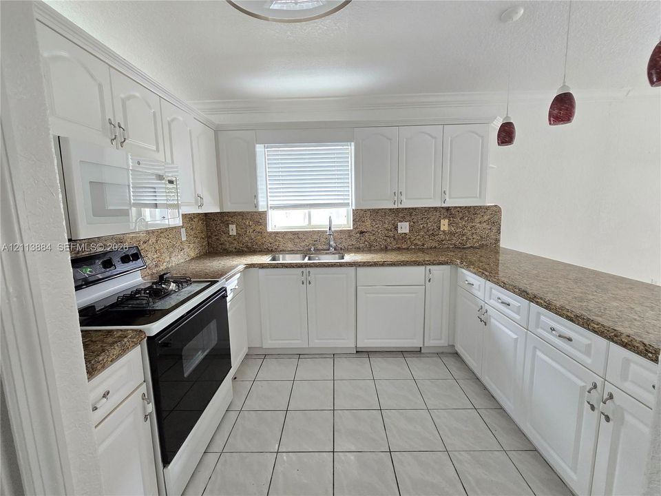 Kitchen featuring white cabinetry, stone-finish countertops, tile flooring, dual-basin sink, and integrated microwave