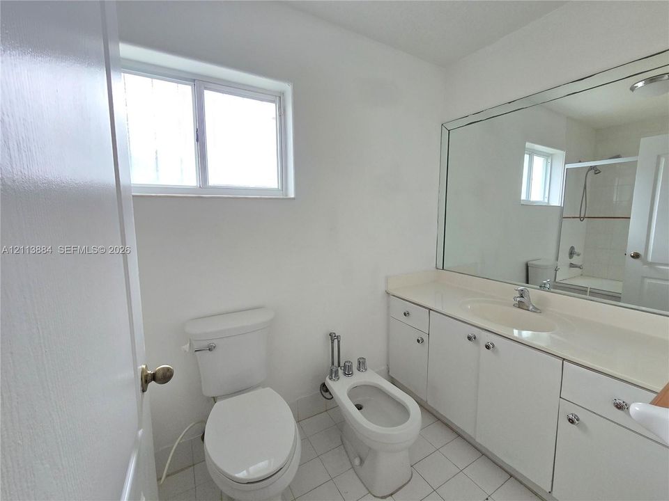 Bathroom featuring white cabinetry, integrated vanity countertop with sink, wall-spanning mirror, bidet, and tile flooring
