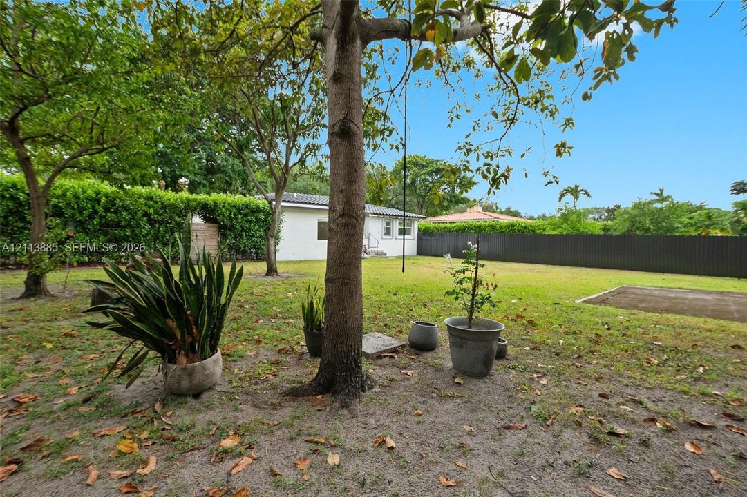 Expansive backyard featuring mature trees, a manicured lawn, perimeter fencing, and a concrete pad