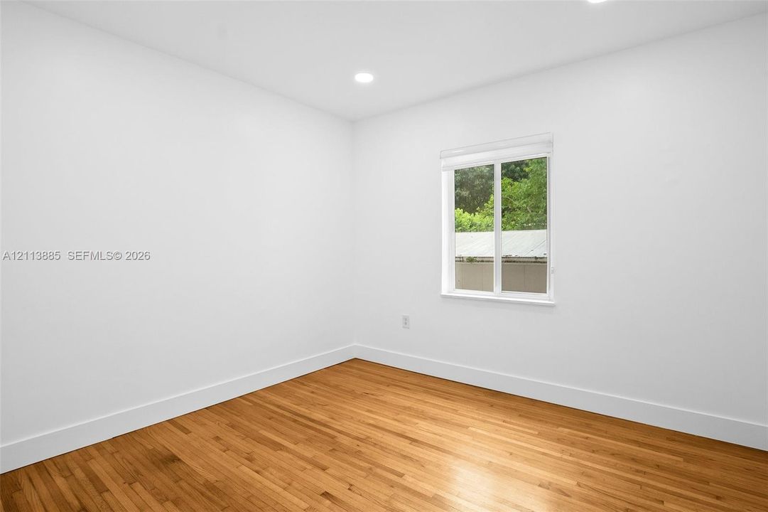 Room interior featuring wood-finish flooring, white walls, recessed ceiling lighting, and a window with a retractable shade
