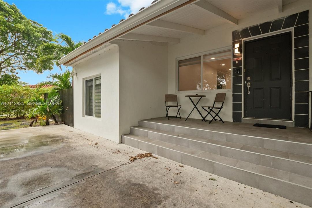 Covered front porch featuring tile flooring and multi-step entry, highlighted by a dark-toned entry door with stone-finish trim and a wide-pane window