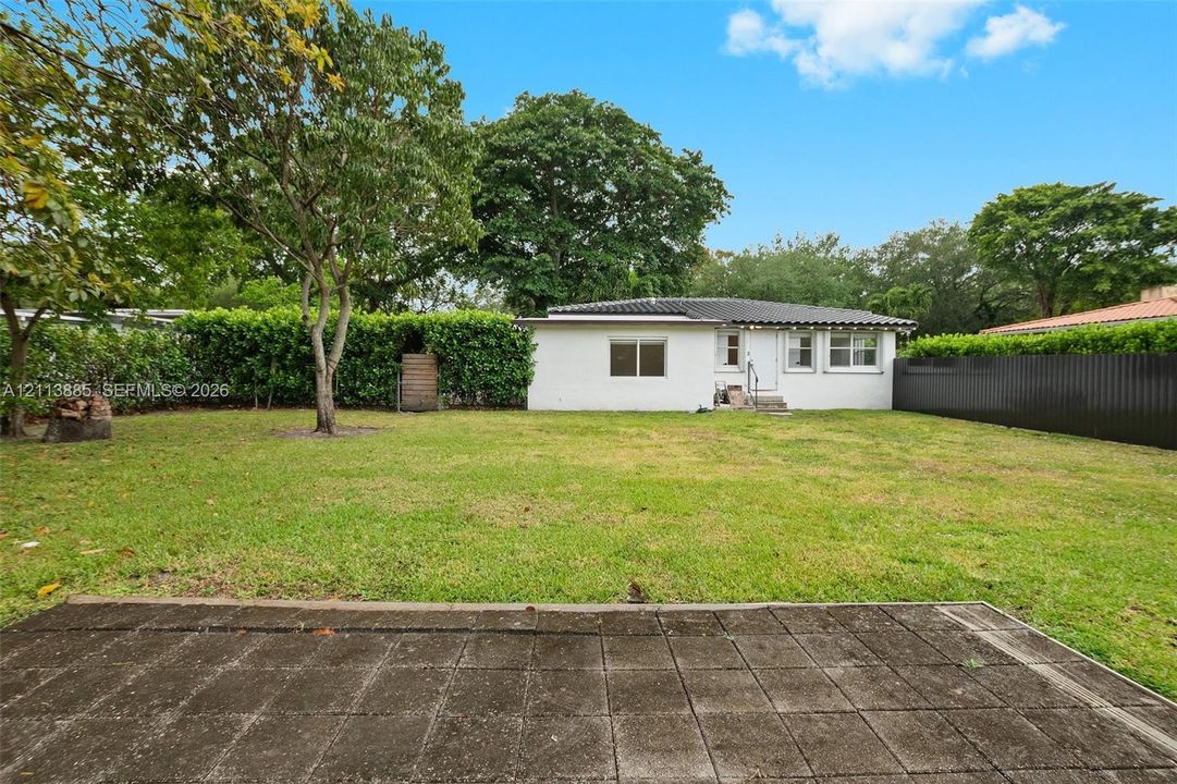 Expansive backyard featuring a concrete patio, mature trees, dense perimeter hedging, and a tall privacy fence