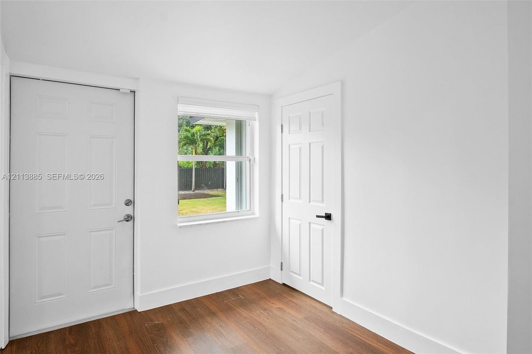 Interior space featuring wood-finish flooring, two six-panel doors with matte black hardware, and a single-hung window with exterior landscape exposure