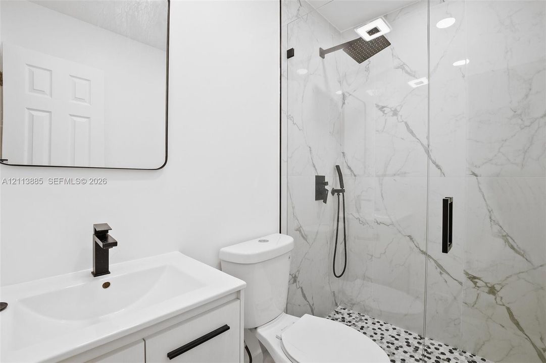 Bathroom featuring a vanity with a single-basin sink, matte black faucet, and framed mirror, paired with a glass-enclosed shower featuring large-format wall tile, a rainfall showerhead, a handheld sprayer, and mosaic floor tile
