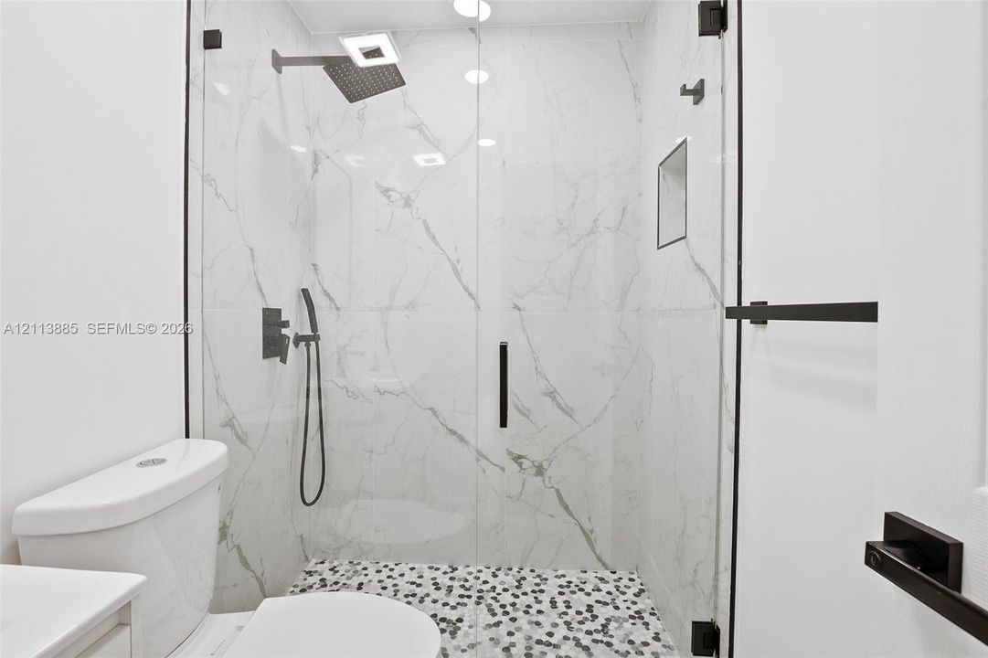 Walk-in shower featuring floor-to-ceiling stone-pattern tile, a glass enclosure, matte black fixtures, a rainfall showerhead, and a mosaic pebble shower floor
