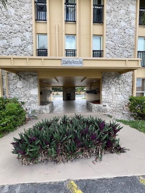 Building exterior featuring stone masonry cladding, a covered porte-cochère, and a landscaped garden bed
