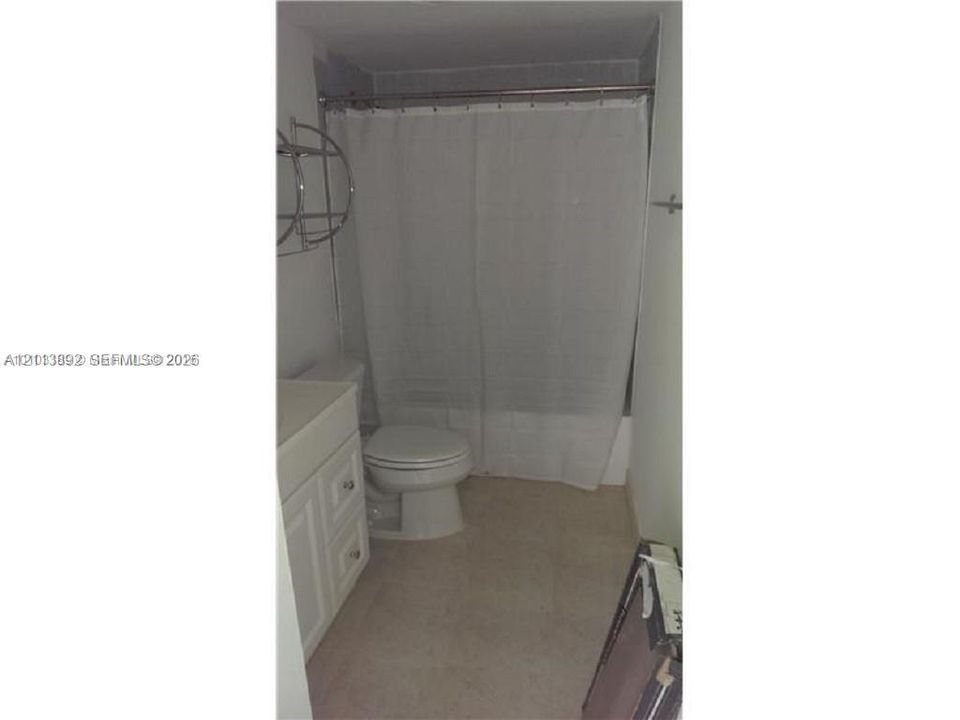 Bathroom featuring a white vanity cabinet with drawers, a toilet, and a tub-shower combination with a metal tension rod