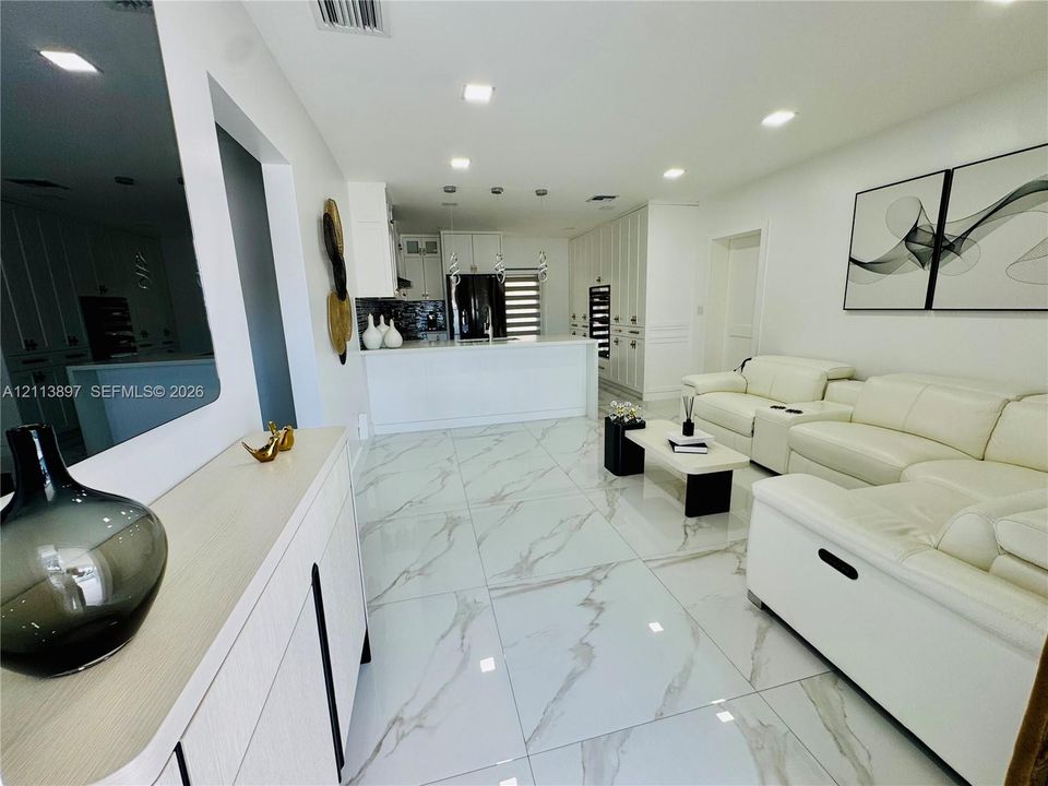 Large-format, light-toned stone-finish floor tiling, white cabinetry with integrated appliances, stone-topped kitchen island, and recessed ceiling lighting