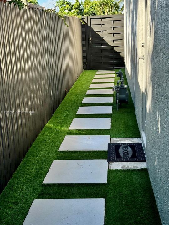 Side yard featuring artificial turf, concrete paver pathway, and metal privacy fencing with a matching pedestrian gate