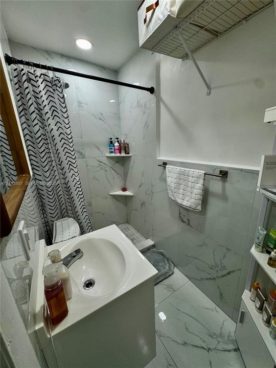 Full-height tiled shower and floor surround with a white stone-pattern finish, recessed shelving, built-in wire storage rack, and wall-mounted metal towel bar
