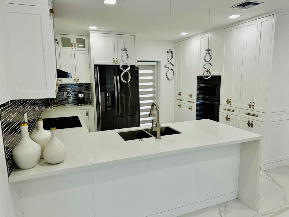 Kitchen featuring white shaker-style cabinetry, quartz countertops, a central island with an undermount sink, built-in wall oven, and geometric pendant lighting