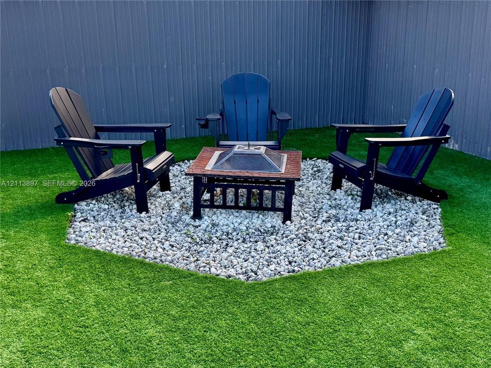 Outdoor area featuring synthetic turf, a hexagonal gravel patio, and corrugated metal fencing
