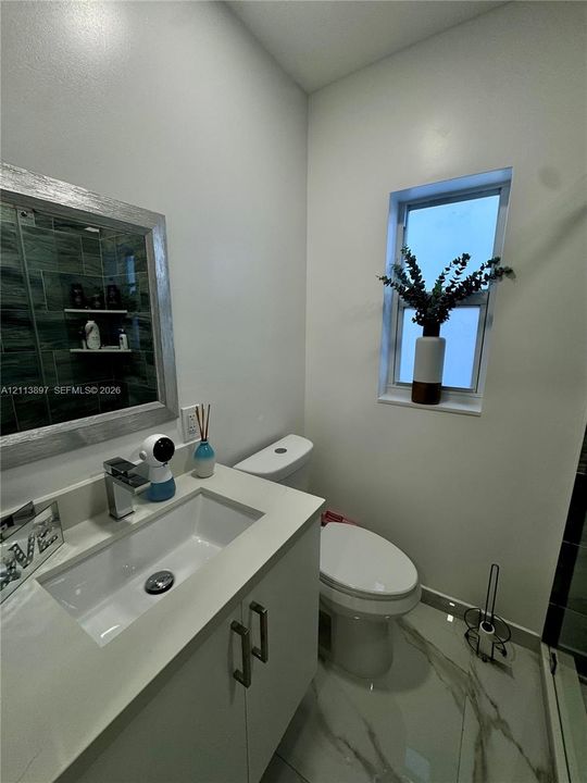 Bathroom featuring a vanity with a white rectangular sink and countertop, framed mirror, stone-finish floor tiling, and a vertical window