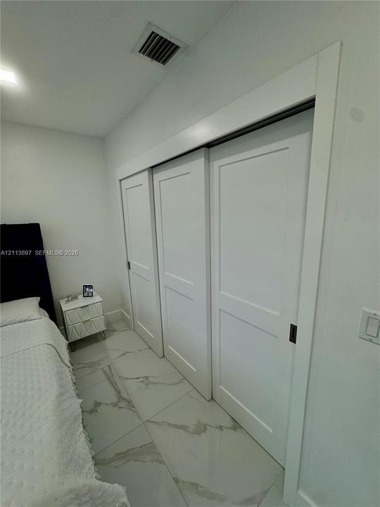 Large-format tile flooring with veining detail and triple-panel sliding closet doors with flush hardware
