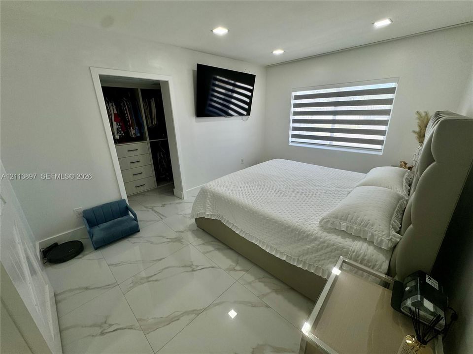 Large-format tile flooring, recessed ceiling lighting, and a walk-in closet featuring built-in shelving and drawer storage