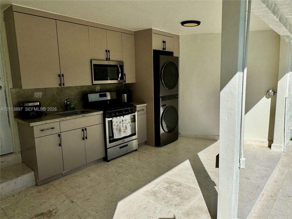 Kitchenette featuring flat-panel cabinetry, stone-finish countertops, stainless steel appliances, and stacked laundry unit, complemented by tile flooring