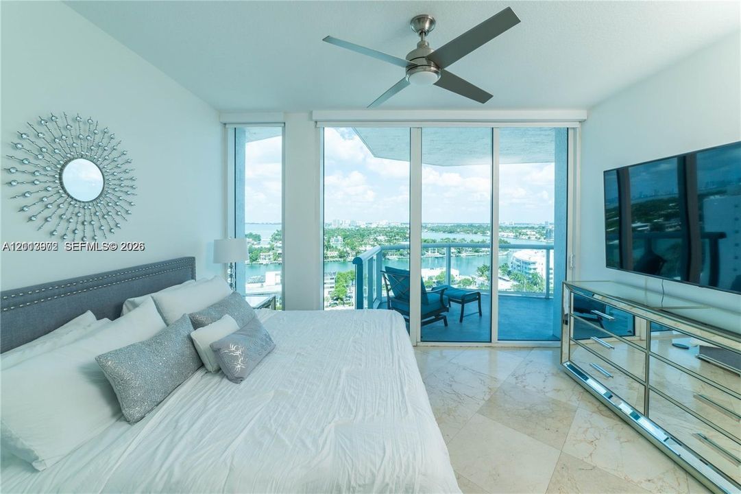 Floor-to-ceiling glass sliding doors, polished stone flooring, balcony access, and a ceiling-mounted fan