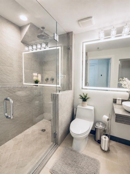 Walk-in shower with floor-to-ceiling stone-finish tile, glass enclosure, rainfall showerhead, and integrated wall niche