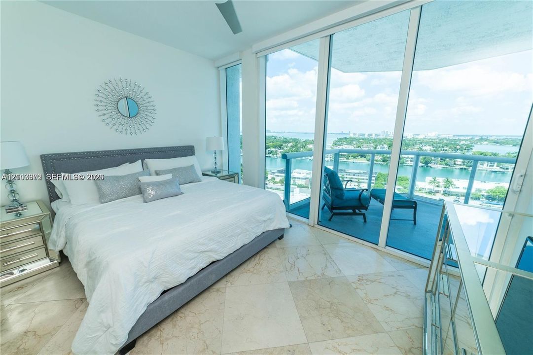 Floor-to-ceiling sliding glass doors, private balcony with glass railing, large-format stone flooring, and ceiling fan