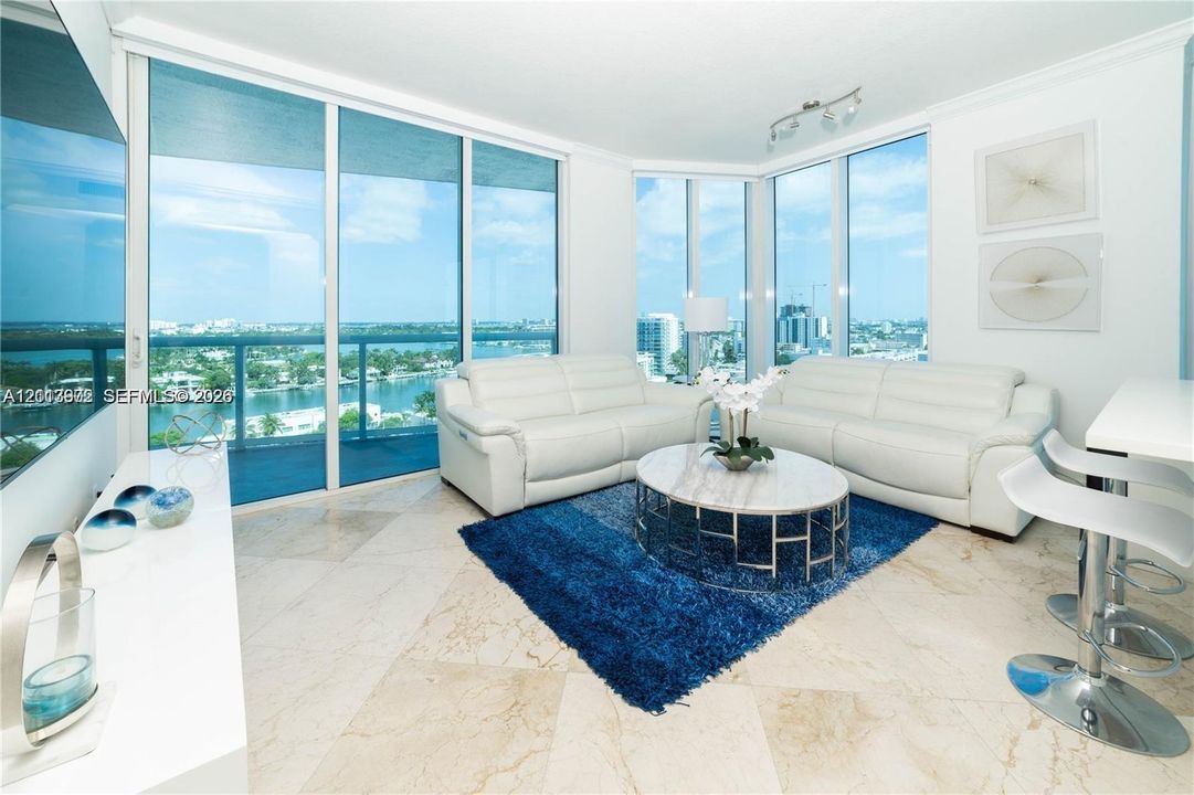 Floor-to-ceiling glass walls, wrap-around balcony access, stone tile flooring, and multi-directional panoramic water scenery