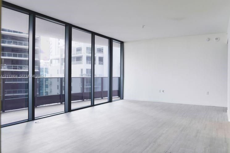 Floor-to-ceiling windows featuring dark frames, wood-finish flooring, and a glass-paneled exterior balcony